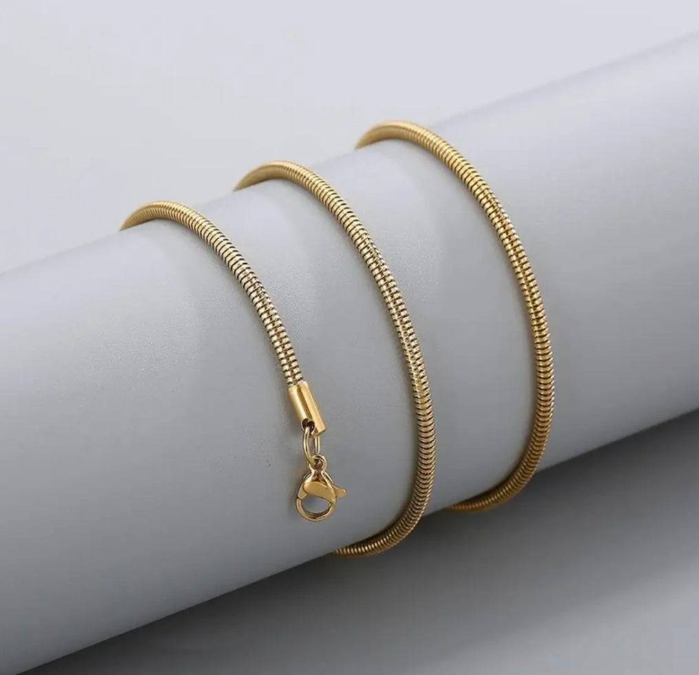 Elegant gold-plated stainless steel snake chain coiled neatly on a white cylindrical surface. Unisex design suitable for any outfit.